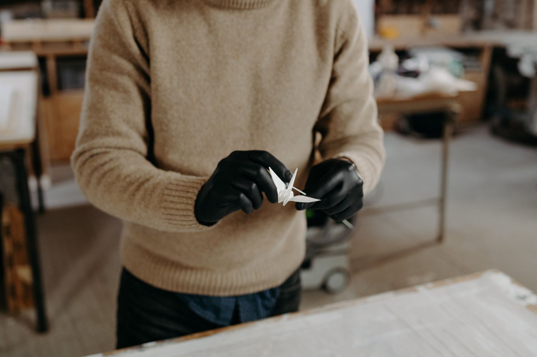 A white paper crane between two gloved hands.