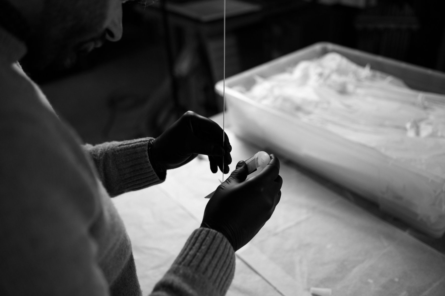 Black-and-white photo of gloved hands fixing a crane to its rod.