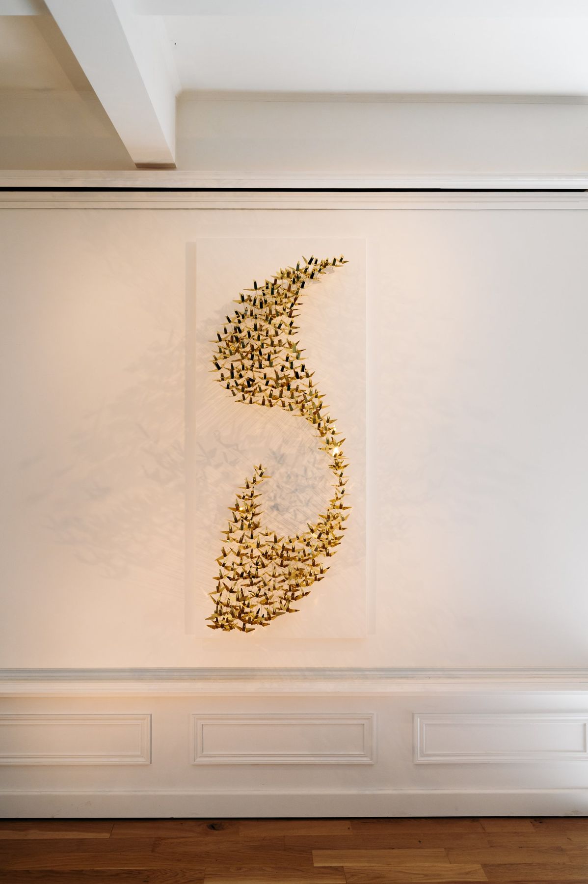 The brass Murmuration hung on a wall with mouldings.