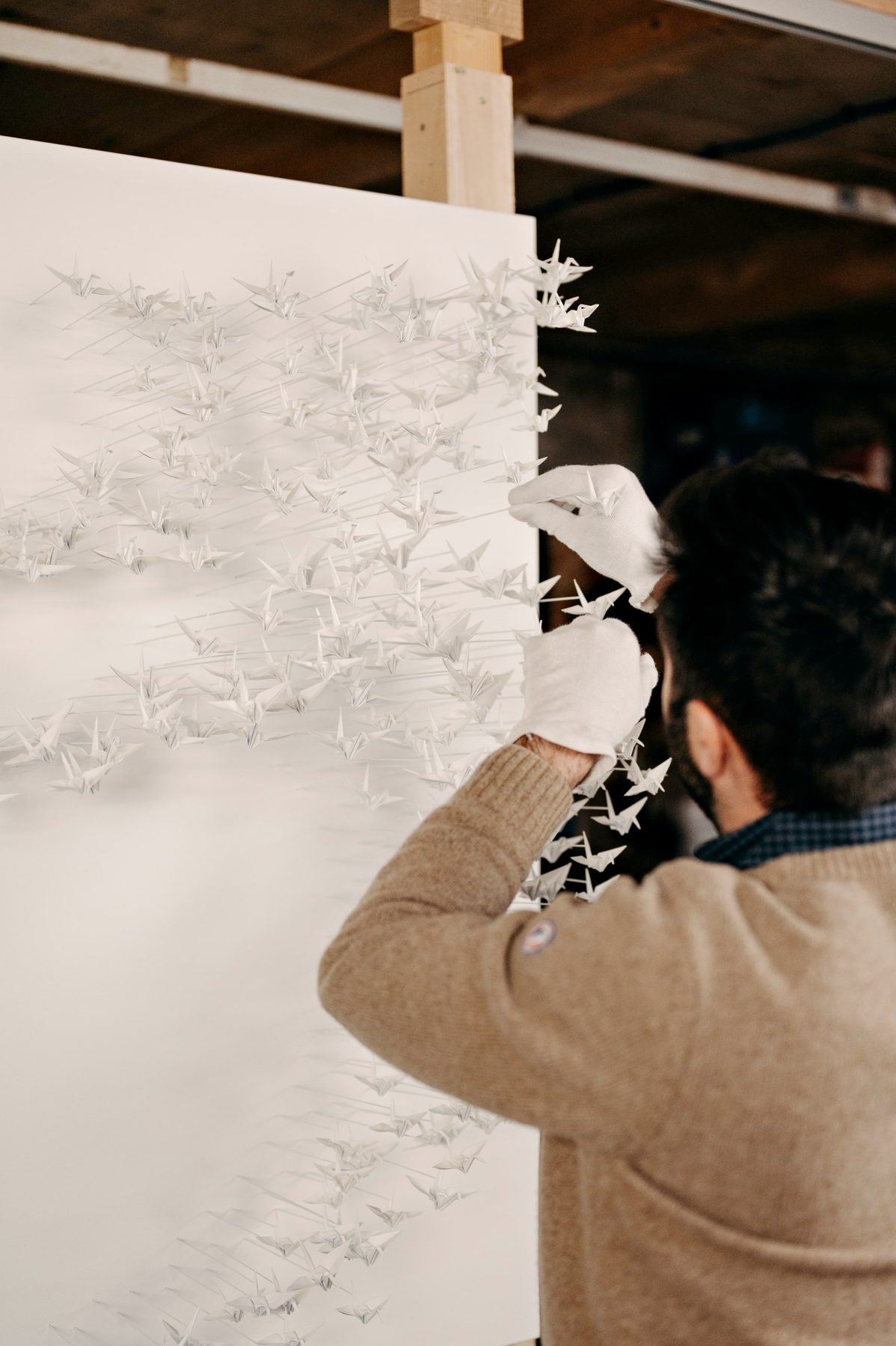 Benjamin Gaumard, in white gloves, places a paper crane on a panel.