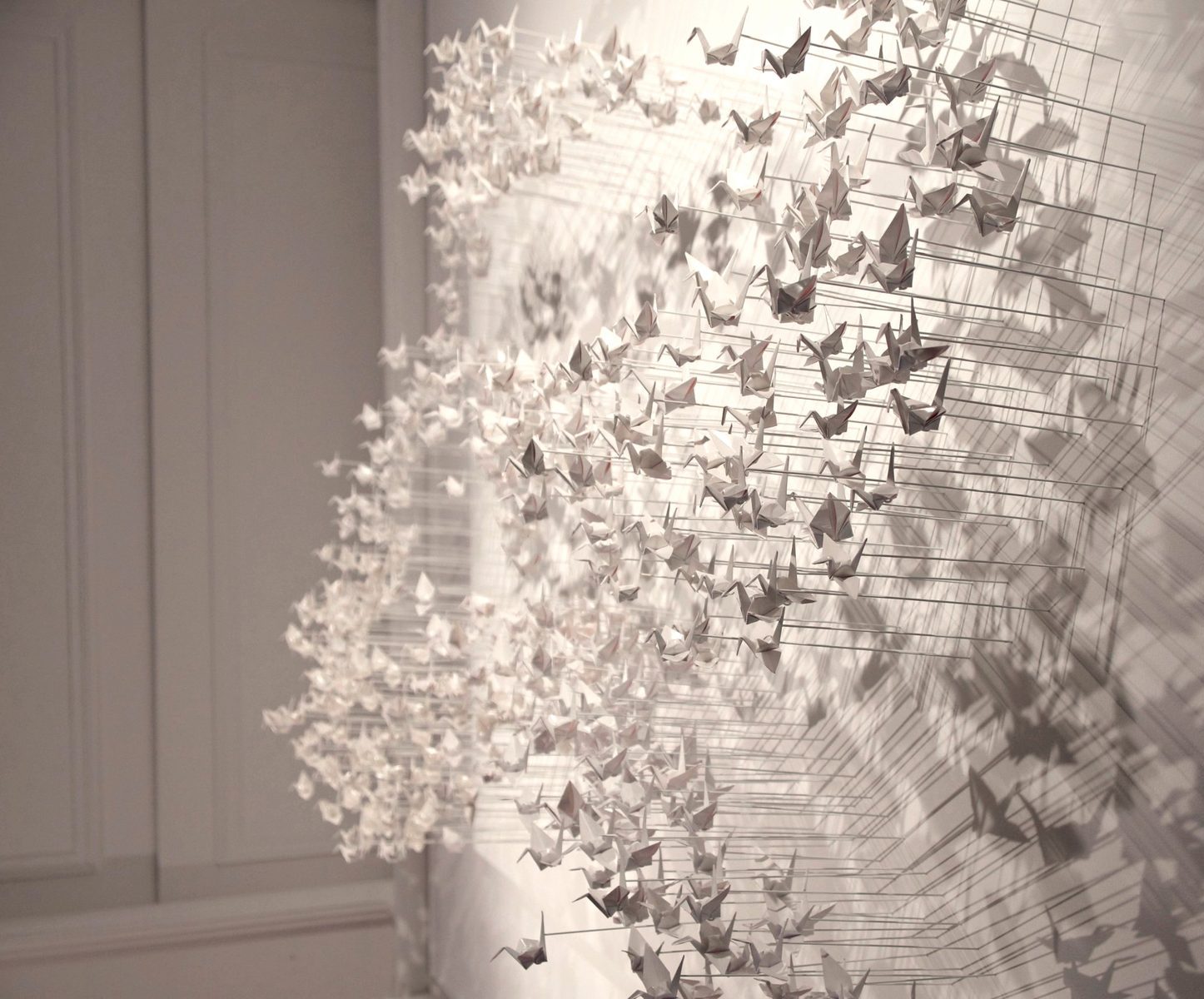 Paper cranes in three-quarter view, sharp in the foreground and blurred behind, with their shadows.