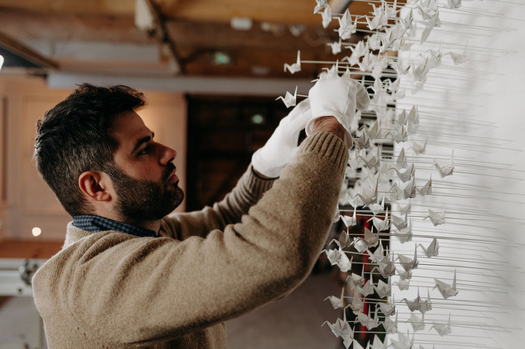 Benjamin Gaumard placing paper cranes, wearing white gloves.